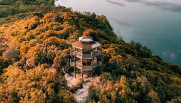 Aerial view of a cabin beside a lake surrounded by autumn trees